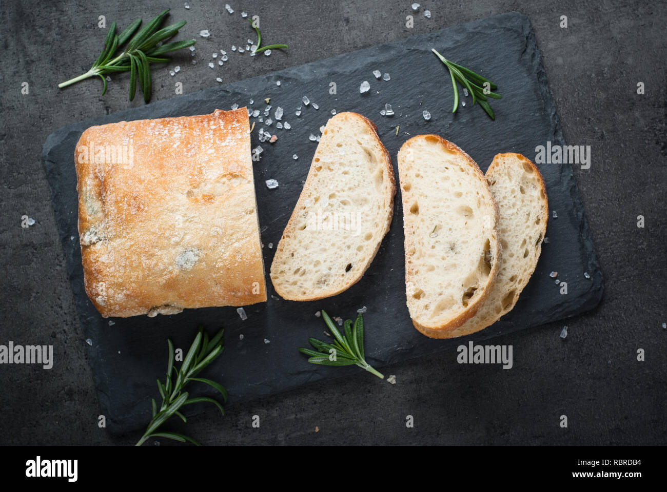 Italienische ciabatta Brot auf schwarzem Schiefer mit Kräutern und Oliven, Ansicht von oben. Stockfoto