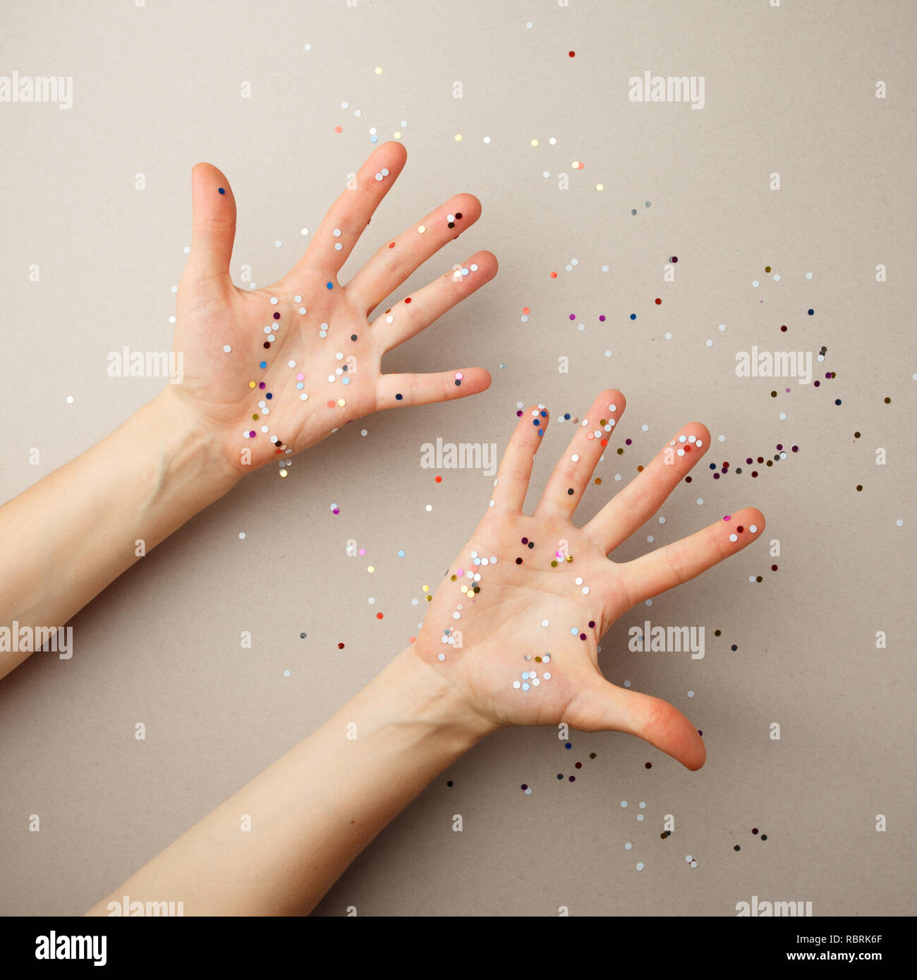 Weibliche Palmen in bunten und gold Konfetti. Grau urlaub Hintergrund mit Lametta. Feier, Party Konzept. Expressive Hände. Ansicht von oben Stockfoto