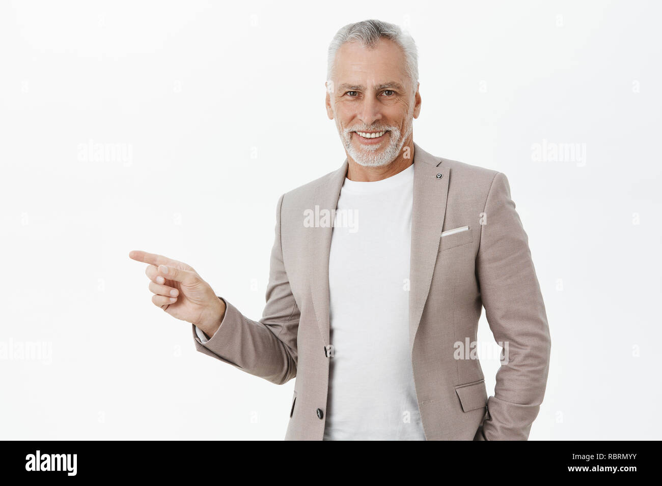 Grandfater Einladen von Gästen in faszinierende colection zu suchen. Elegante und Selbst - gut versichert - Suchen weisen alten Mann im Anzug mit grauen Bart und Haar nach rechts und lächelt mich an Kamera Stockfoto
