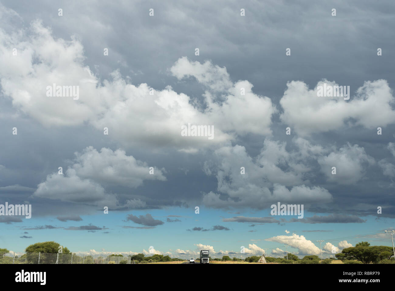 Cumulus oder geschwollene Wolken am Himmel und unten eine lange Straße, die sich in die Unendlichkeit mit Fahrzeugen in der North West Provinz von Südafrika Stockfoto