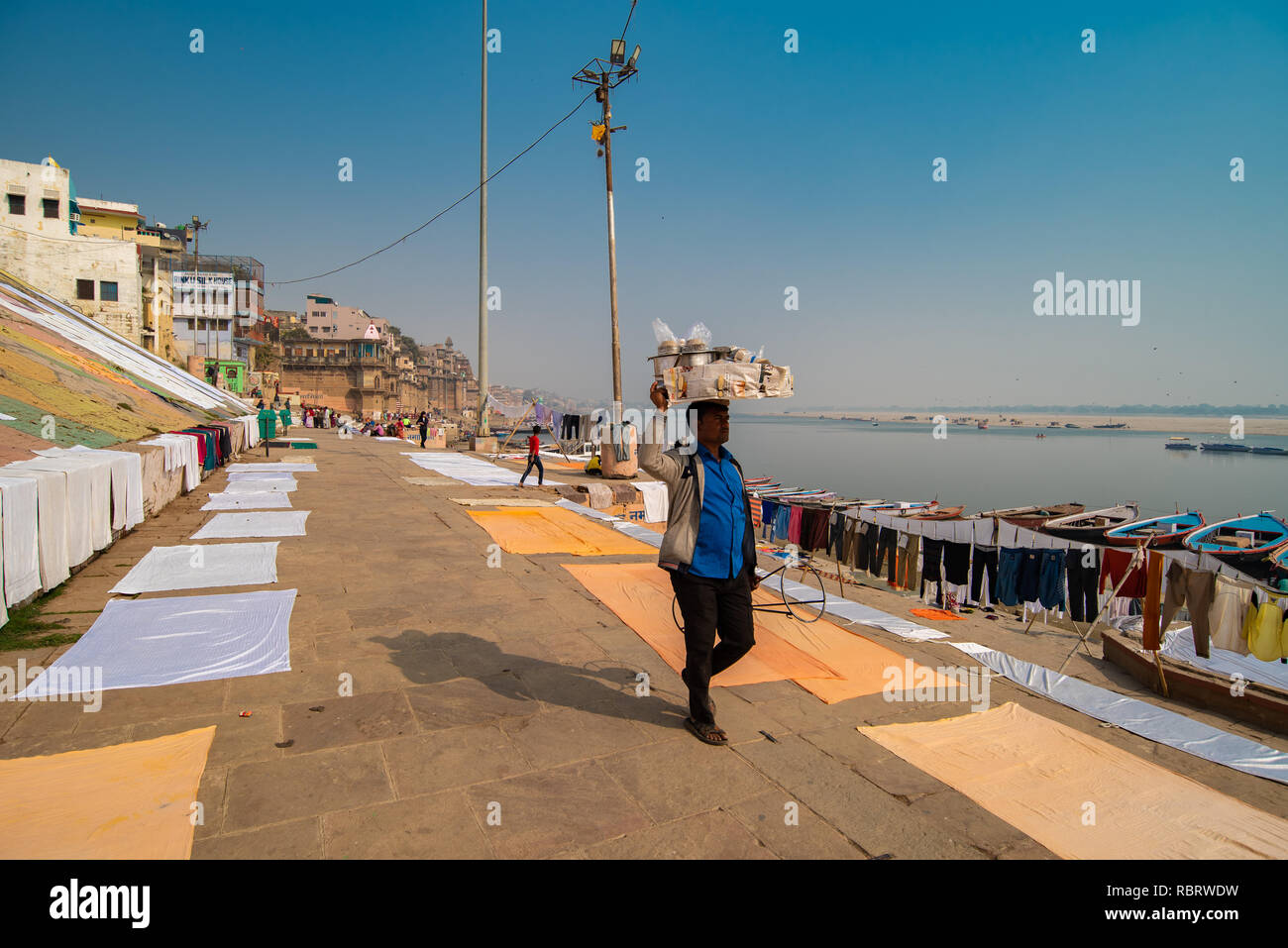Street Hawker trägt seine Waren auf dem Kopf beim Wandern entlang des Ganges in Varanasi, Indien Stockfoto
