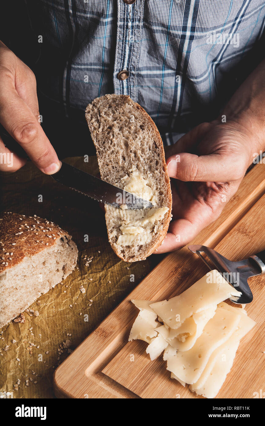 Vorbereitung gesunde vegetarische Bruschetta auf rustikalen Holztisch. Ansicht von oben auf die männliche Hände Verbreitung Frischkäse auf Roggen Vollkornbrot. Die Sandwiches für Snack Stockfoto