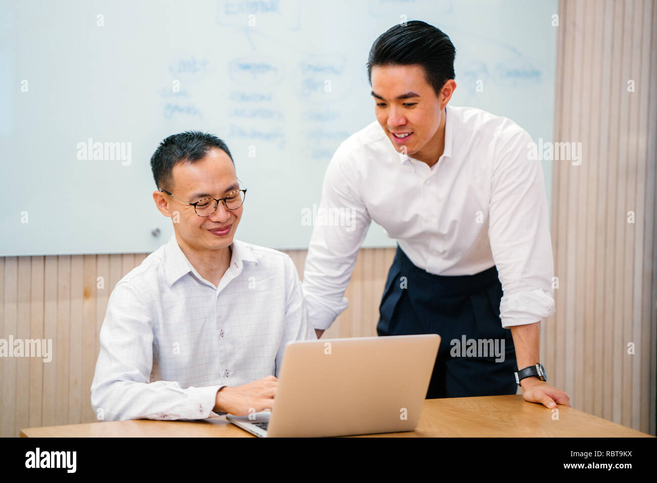 Porträt von zwei asiatischen Geschäftsleuten, die eine geschäftliche Besprechung in einem Tagungsraum mit einer Tafel im Hintergrund. Sie sind beide auf der Suche nach einem Notebook. Stockfoto