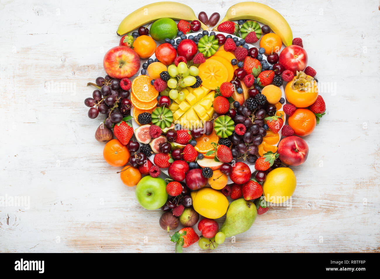 Herz aus gesunden rainbow Obst Schüssel Pflaumen Erdbeeren Himbeeren, Orangen, Äpfel, Kiwis, Weintrauben, Heidelbeeren mango Kaki Ananas Stockfoto