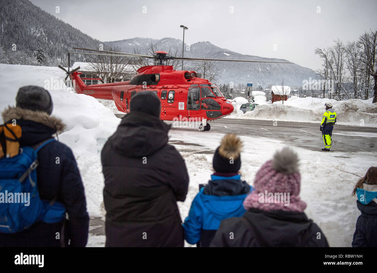 12 Januar 2019, Bayern, Schönau am Königssee: ein Hubschrauber der Stände des Typs "Super Puma" auf einem Parkplatz und wird von den Zuschauern während der Anlaufphase beobachtet. Der Helikopter ist für Wirbel der Schnee von den Bäumen auf Straßen soll und damit das Risiko einer Niederlassung Bruch zu reduzieren. Die starken Schneefälle der vergangenen Tage weiterhin den Einsatzkräften in Atem im südlichen Bayern und Neuschnee zu halten ist schon näher. Nach Angaben der Behörden mehr als 1000 Helfer sind in den südlichen Bezirken von Oberbayern eingesetzt. Foto: Lino Mirgeler/dpa Stockfoto