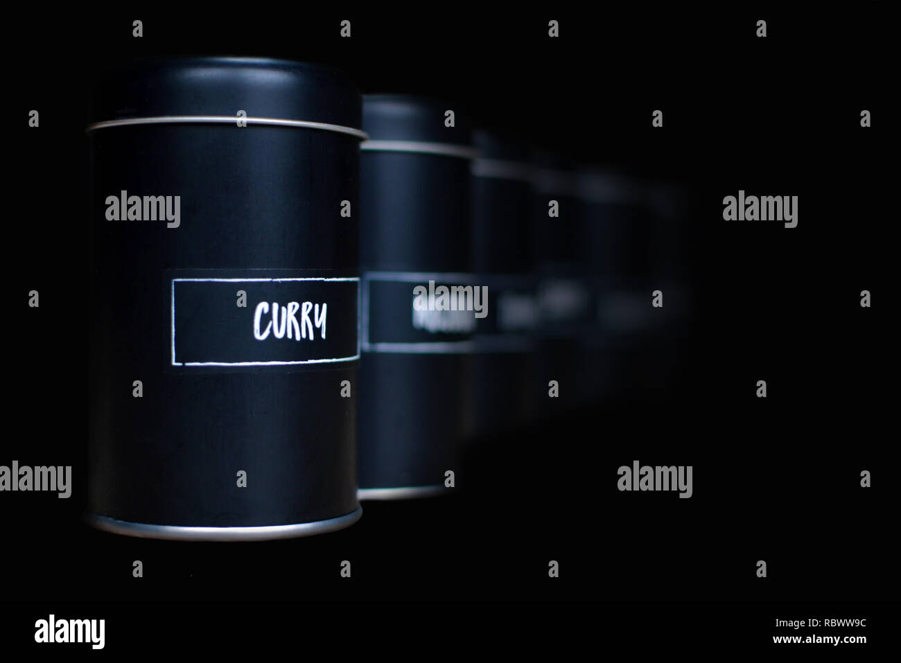Anderen schwarz Spice Shakers in einer Zeile ausblenden auf dunklem Hintergrund mit weißem Label Curry auf der Vorderseite Stockfoto