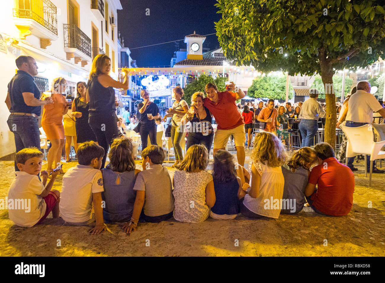 Eltern feiern auf einer Fiesta im dorfplatz, während ihre Kinder um 2 Uhr morgens auf dem Handy sind. Plaza Espana, Carcabuey, Andalusien. Spanien Stockfoto