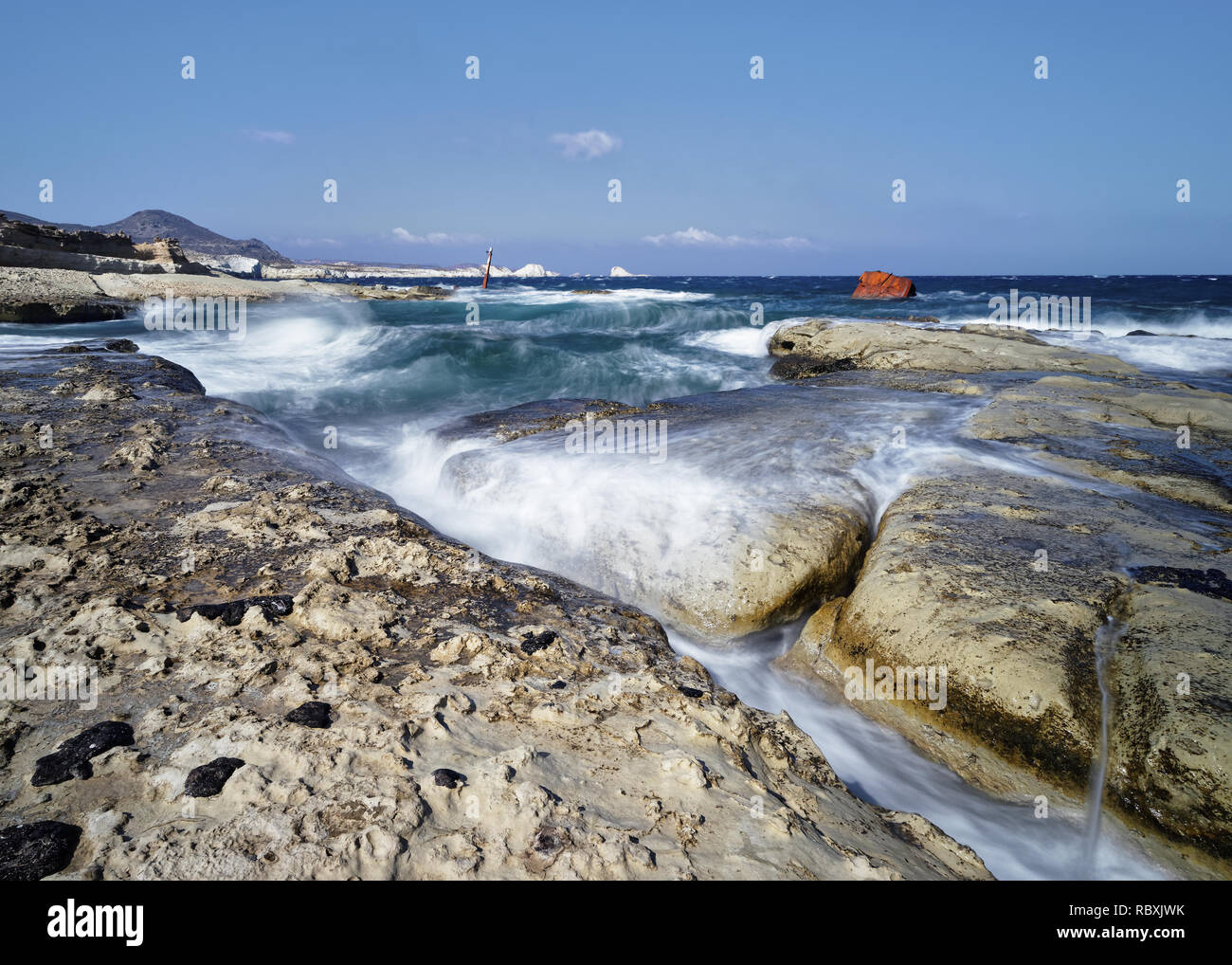 Bei starkem Wind, hohen Wellen über große Platten auf einem Strand von light rock fließen, Wasser Bewegung in lange Exposition, im Hintergrund ein schiffswrack - Ort: Stockfoto