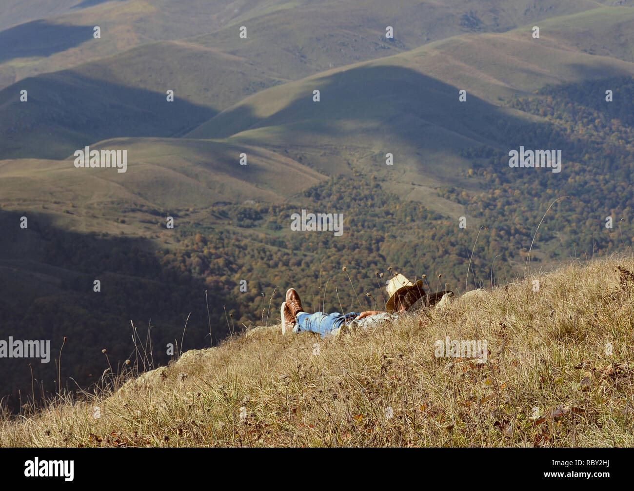 Junger Mann in cowboy Kleidung Rest am Berge. Reisenden mit Panoramablick Blick während der Wanderung, schönen Hintergrund mit Berglandschaft. Stockfoto