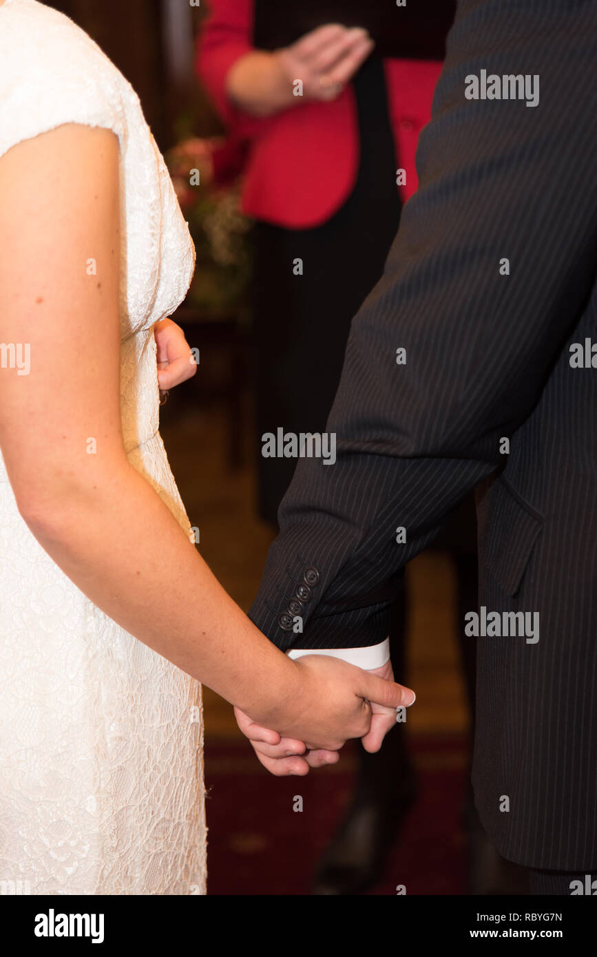 Rückansicht der Braut im weißen Kleid und der Bräutigam in der Klage halten jedes andere Hände Stockfoto