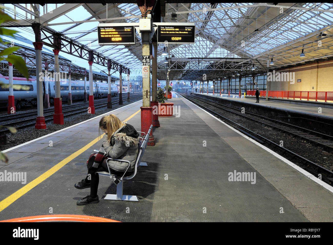 Eine junge Frau auf einer Bank sitzen Warten auf einen Zug auf der Plattform in Crewe Bahnhof in England UK KATHY DEWITT Stockfoto