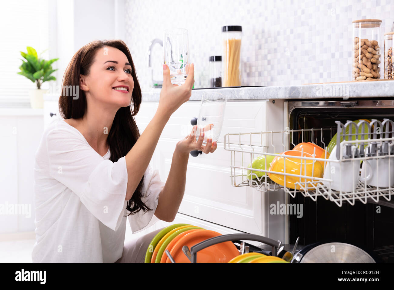 Glückliche junge Frau suchen Bei Trinkgläsern in der Nähe von Spülmaschine Stockfoto