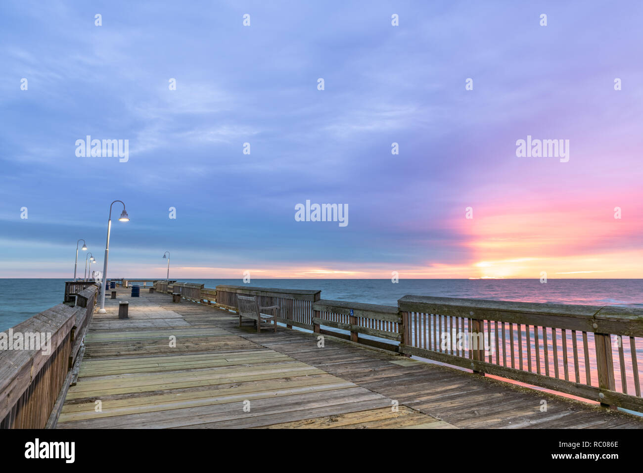 Sonnenaufgang von der Sandbridge Fishing Pier auf der kleinen Insel Park in Virginia Beach. Das Holz der Pier leuchtet durch frühen Morgen Sonne in der Clou Stockfoto