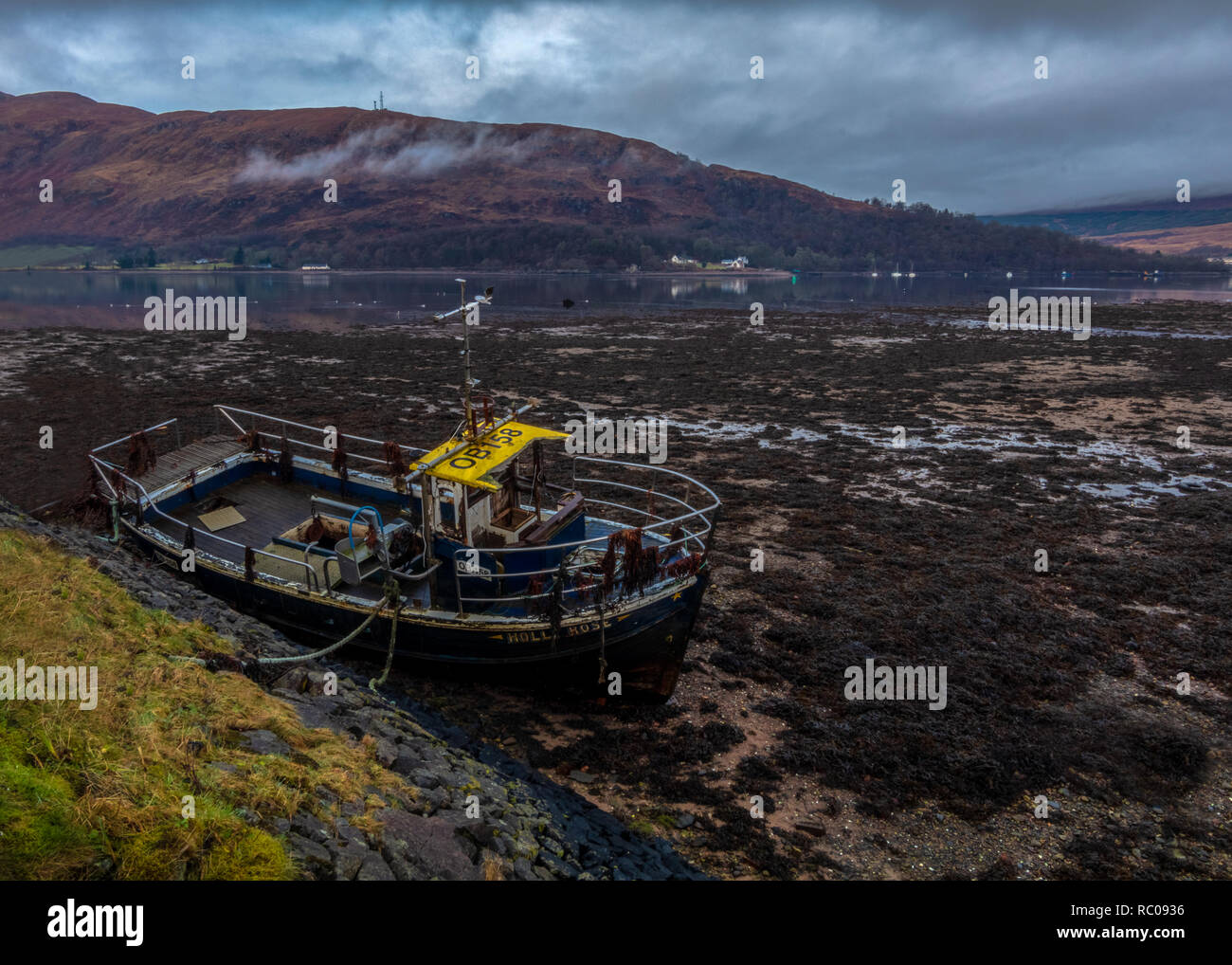 Altes Schiff auf dem trockenen See am frühen Morgen in Fort William, im Norden Schottlands. Bergen im Hintergrund und Grau tiefe Wolken. Stockfoto