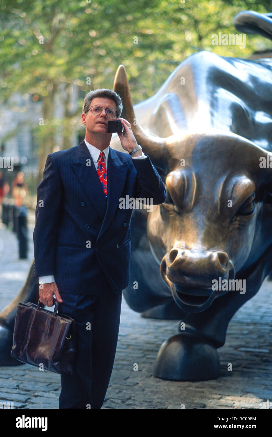 1990 s Geschäftsmann ist auf sein Handy vor der wütenden Stier Statue, Financial District, New York City, USA Stockfoto