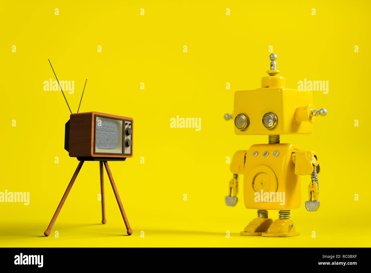Niedliche gelbe handgefertigte Roboter auf einem gelben Hintergrund mit retro Fernsehen. Stockfoto