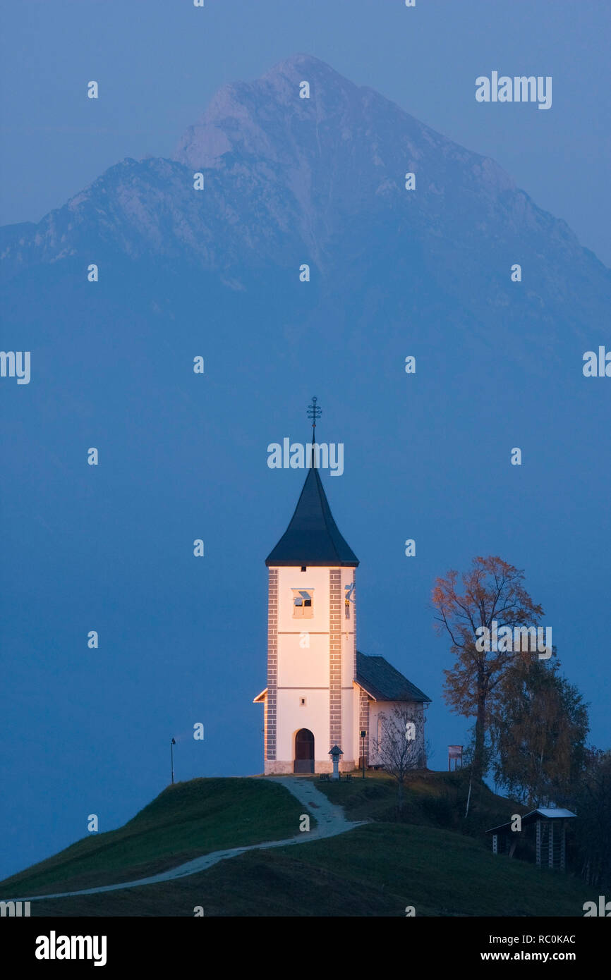 Kirche St. Primoz in der Dämmerung mit der Spitze des Storzic in der Steiner Alpen, Slowenien Stockfoto