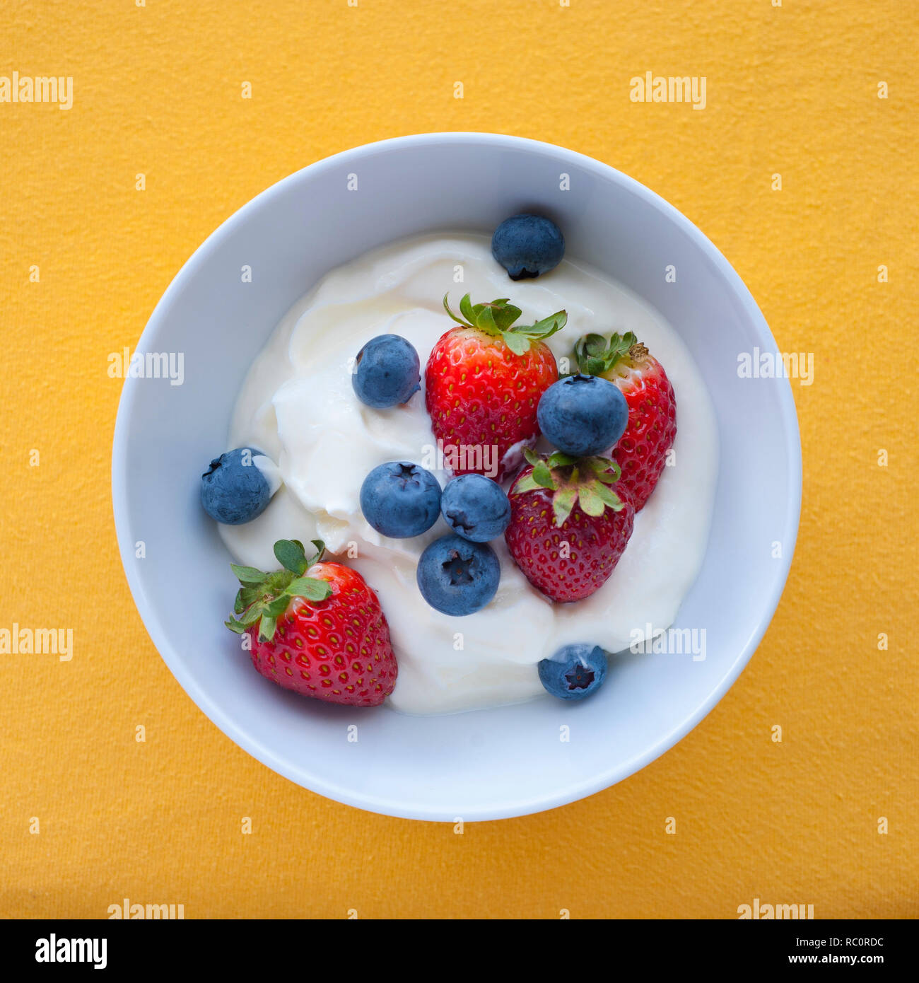 Joghurt mit frischen Erdbeeren und Blaubeeren in Schüssel mit gelbem Hintergrund, Ansicht von oben Stockfoto