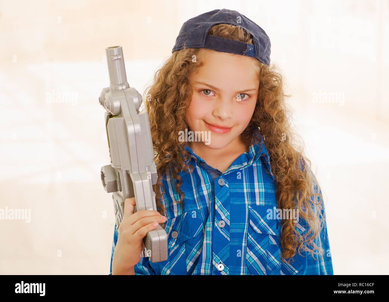 In der Nähe von schönen Curly girl wearin junge Kleidung und halten in ihren Händen ein Spielzeug gewehr Stockfoto