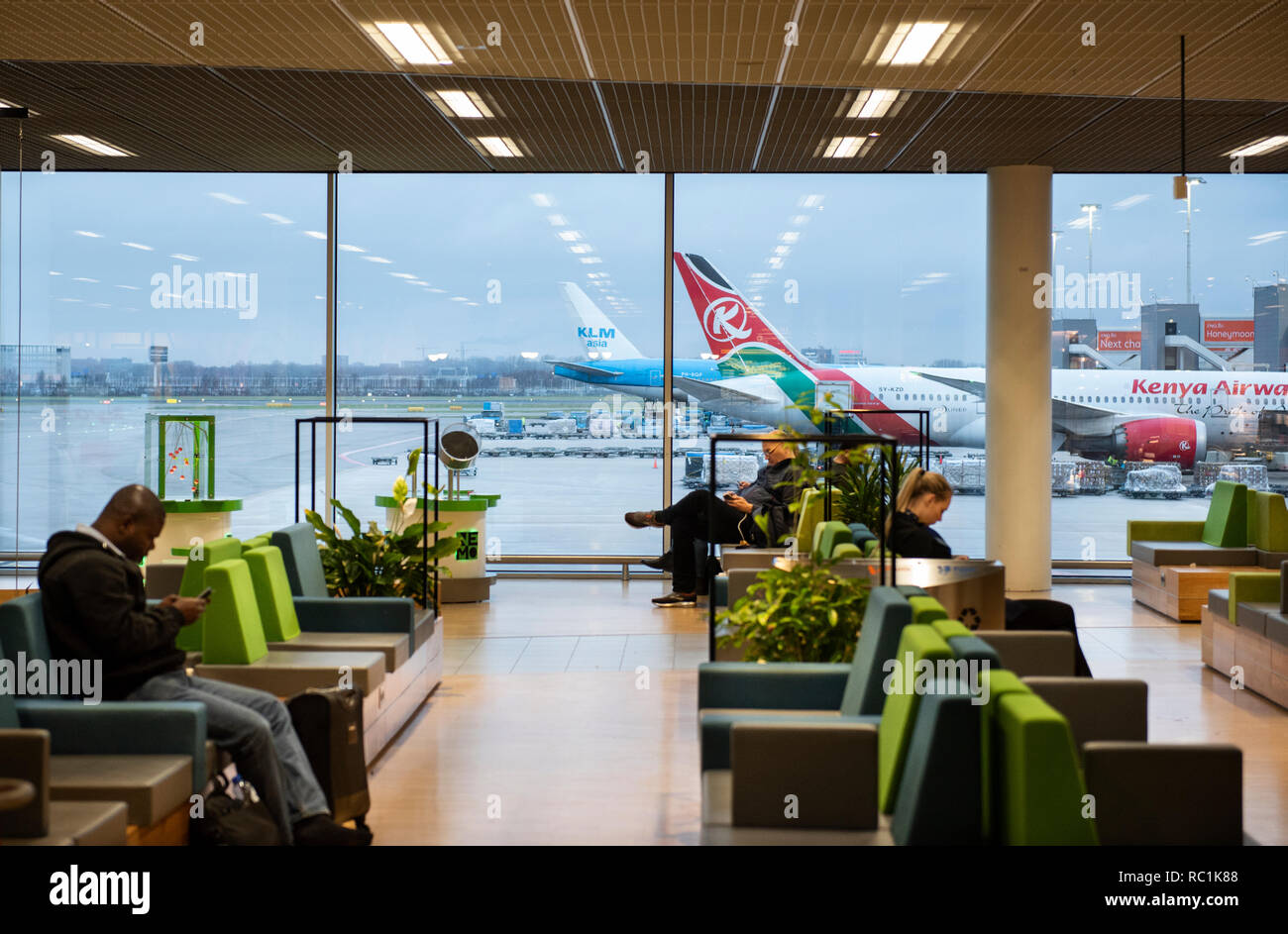 Fahrgäste im Wartebereich an einem Boarding Gate am Flughafen Amsterdam Schiphol sitzen. Stockfoto