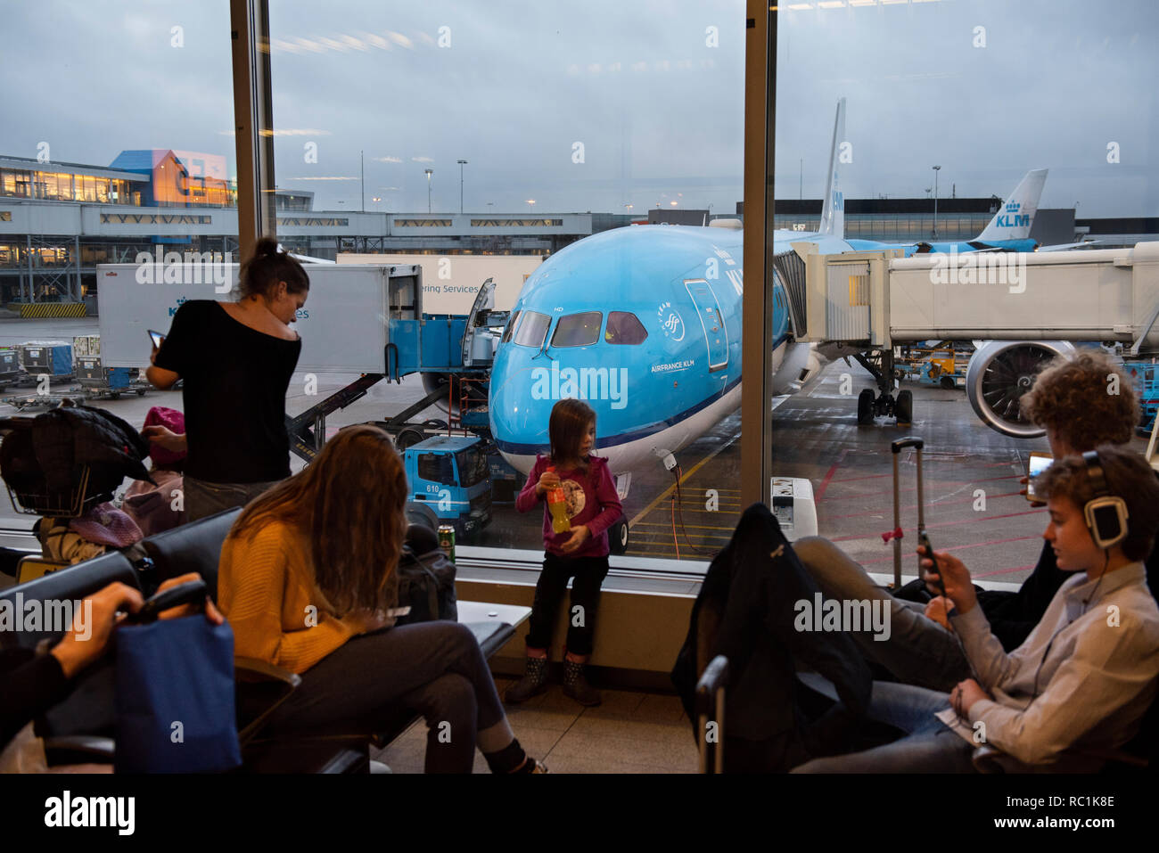 Fahrgäste im Wartebereich an einem Boarding Gate sitzen, neben einem KLM Royal Dutch Airlines Flugzeug in Amsterdam Schiphol Flughafen Landebahn. Stockfoto