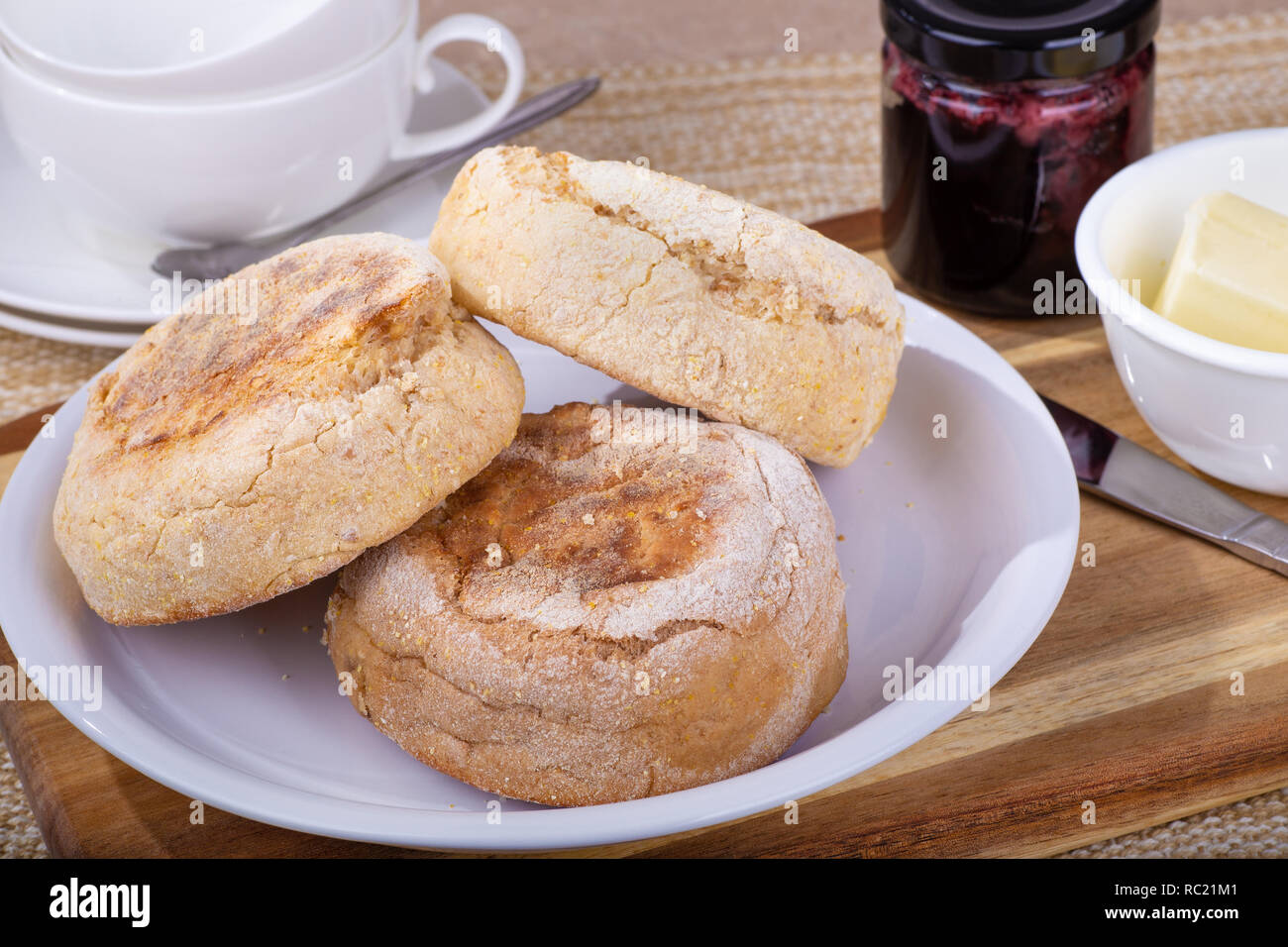 Platte der Englische Muffins die mit Butter und Marmeladenglas auf einem Holzbrett Stockfoto