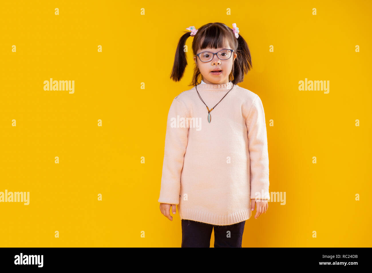 Neugierig kleines Mädchen mit Down-syndrom gegen orange Wand posieren Stockfoto