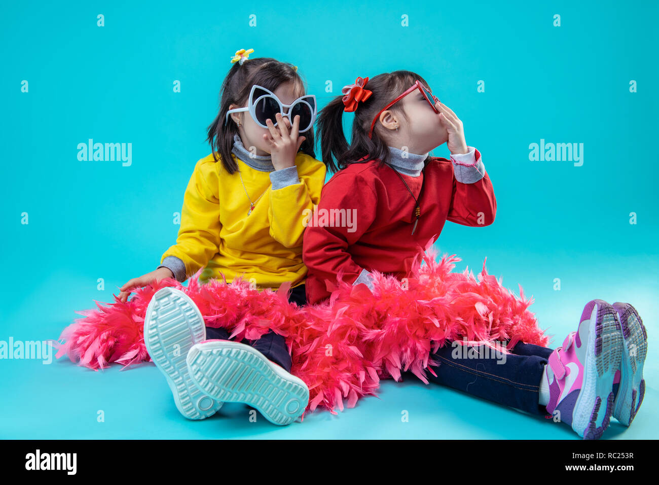 Zwei glückliche Mädchen sitzen auf Studio beim Tragen der Brille Stockfoto