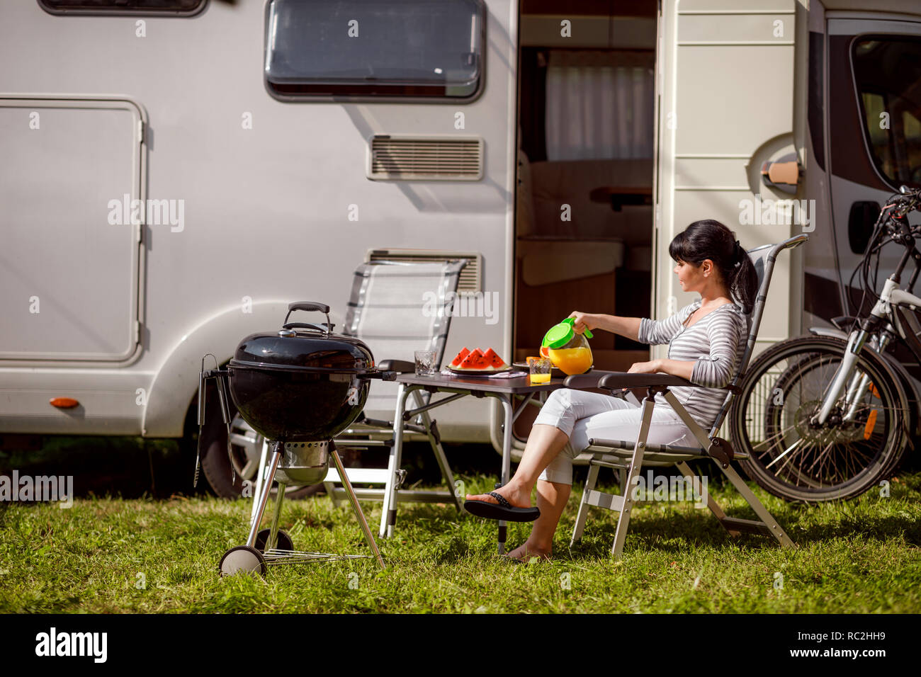 Familienurlaub reisen RV, Urlaub im Reisemobil, Caravan Auto Urlaub. Picknick mit Grill im Freien. Frau gießt aus einem Glas Orangensaft Stockfoto Familienurlaub reisen RV, Urlaub im Reisemobil, Caravan Auto Urlaub. Picknick mit Grill im Freien. Frau gießt aus einem Glas Orangensaft Stockfoto