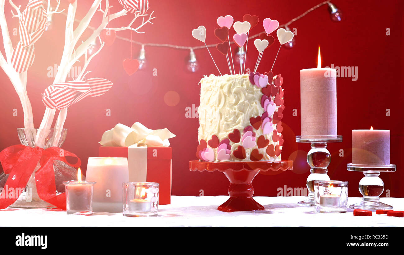 Schönen Valentinstag party Tisch mit Showstopper rot, weiß und rosa Herzen Double Layer Cake, mit weißer Schokolade Zuckerguss, mit Lens flare Stockfoto