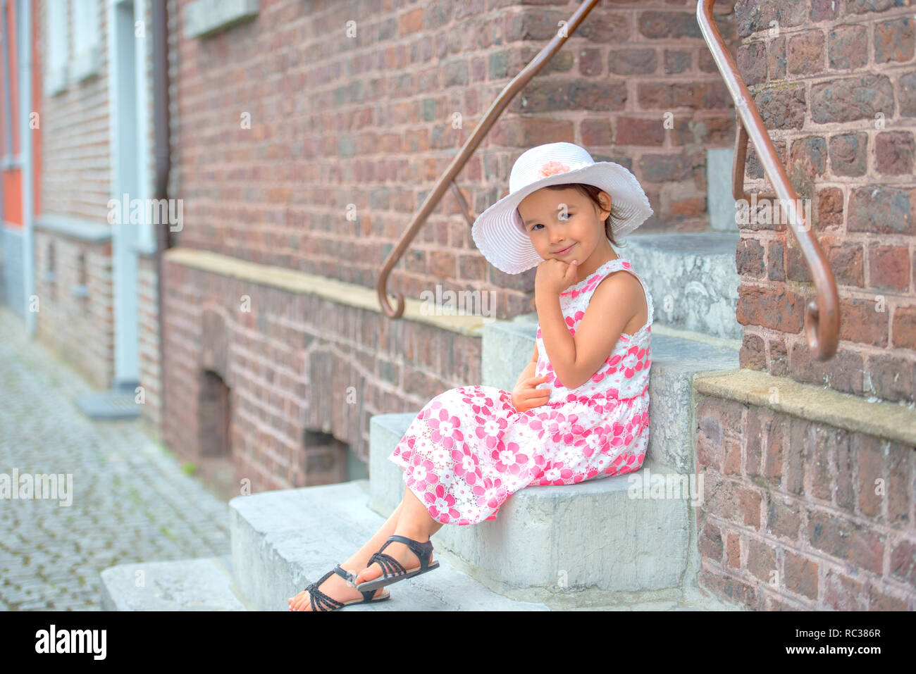Adorable kleine Mädchen mit weißen Hut sitzt auf der Treppe, an warmen und sonnigen Sommer Tag Stockfoto
