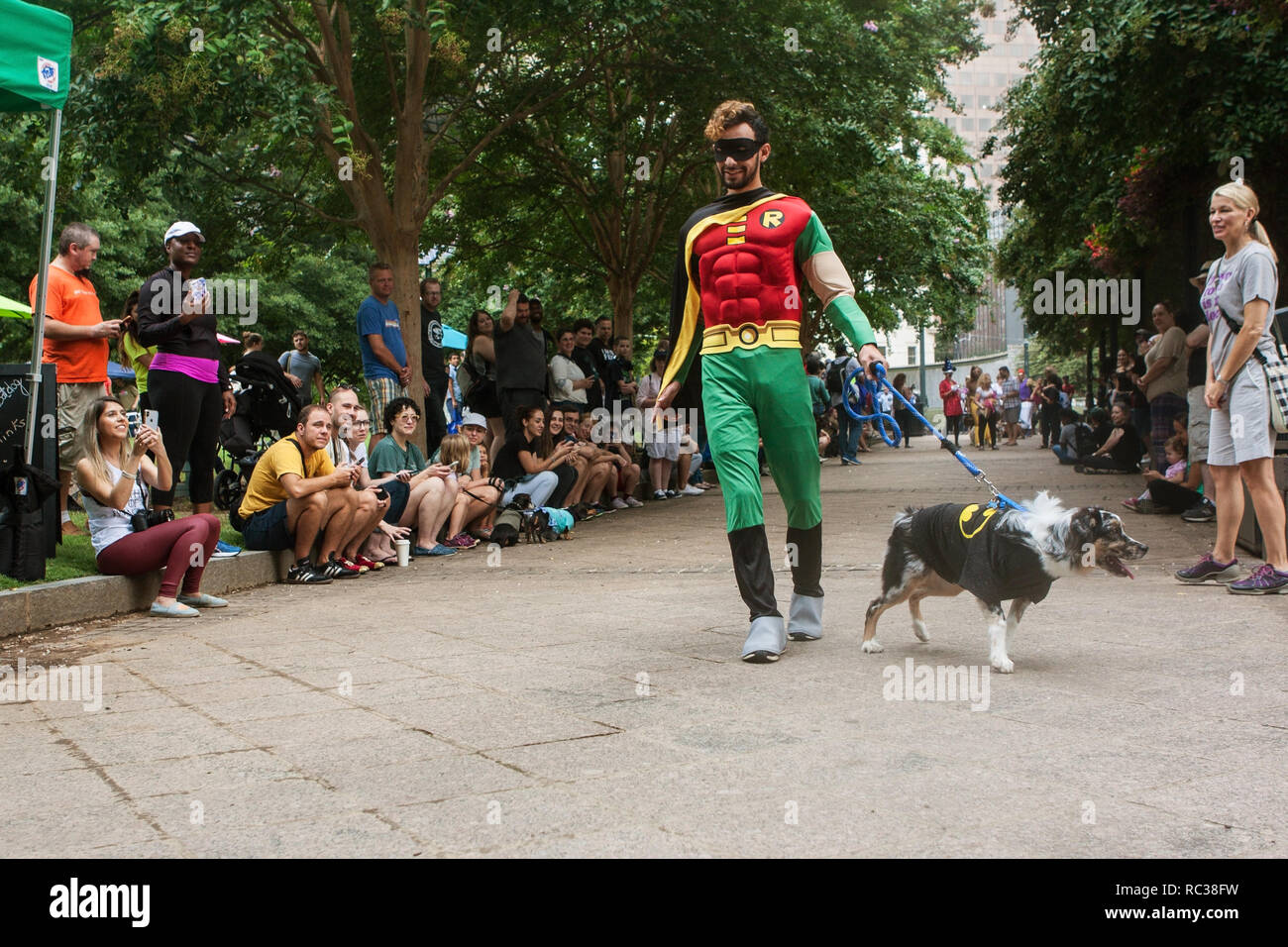 Ein Mann mit einem Robin Kostüm geht seinen Hund trägt ein Batman Kostüm vor der Masse von Zuschauern bei Doggy Con, ein Hund Kostümwettbewerb in Atlanta. Stockfoto