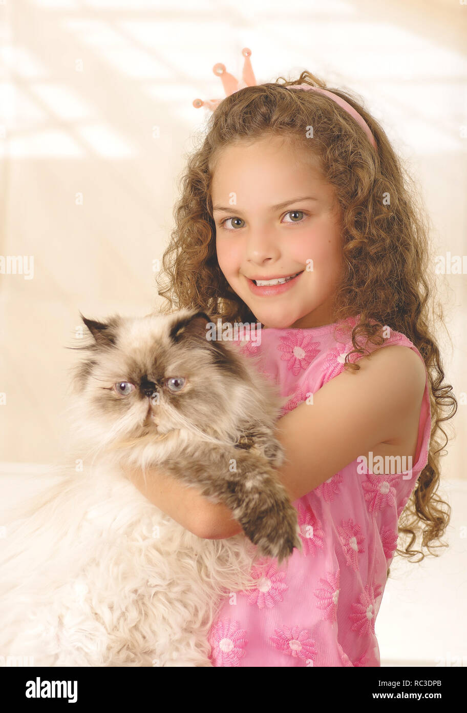Schöne kleine lockige Mädchen umarmte ihre Katze und das Tragen eines Pink Princess Dress Stockfoto