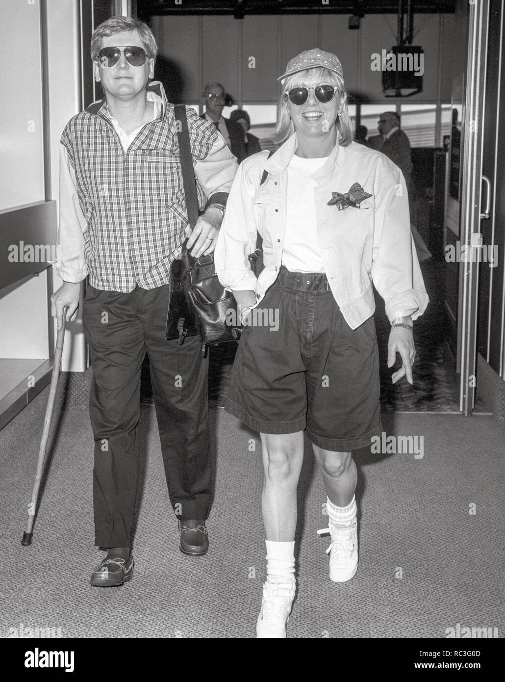 Britische Fernsehmoderatorin Mike Smith (Schmiede) und Frau Sarah Greene verlassen den Flughafen Heathrow in 1989. Mike Smith war noch mit der Hilfe von einem Stock nach dem Absturz eines Hubschraubers im Vorjahr. Stockfoto