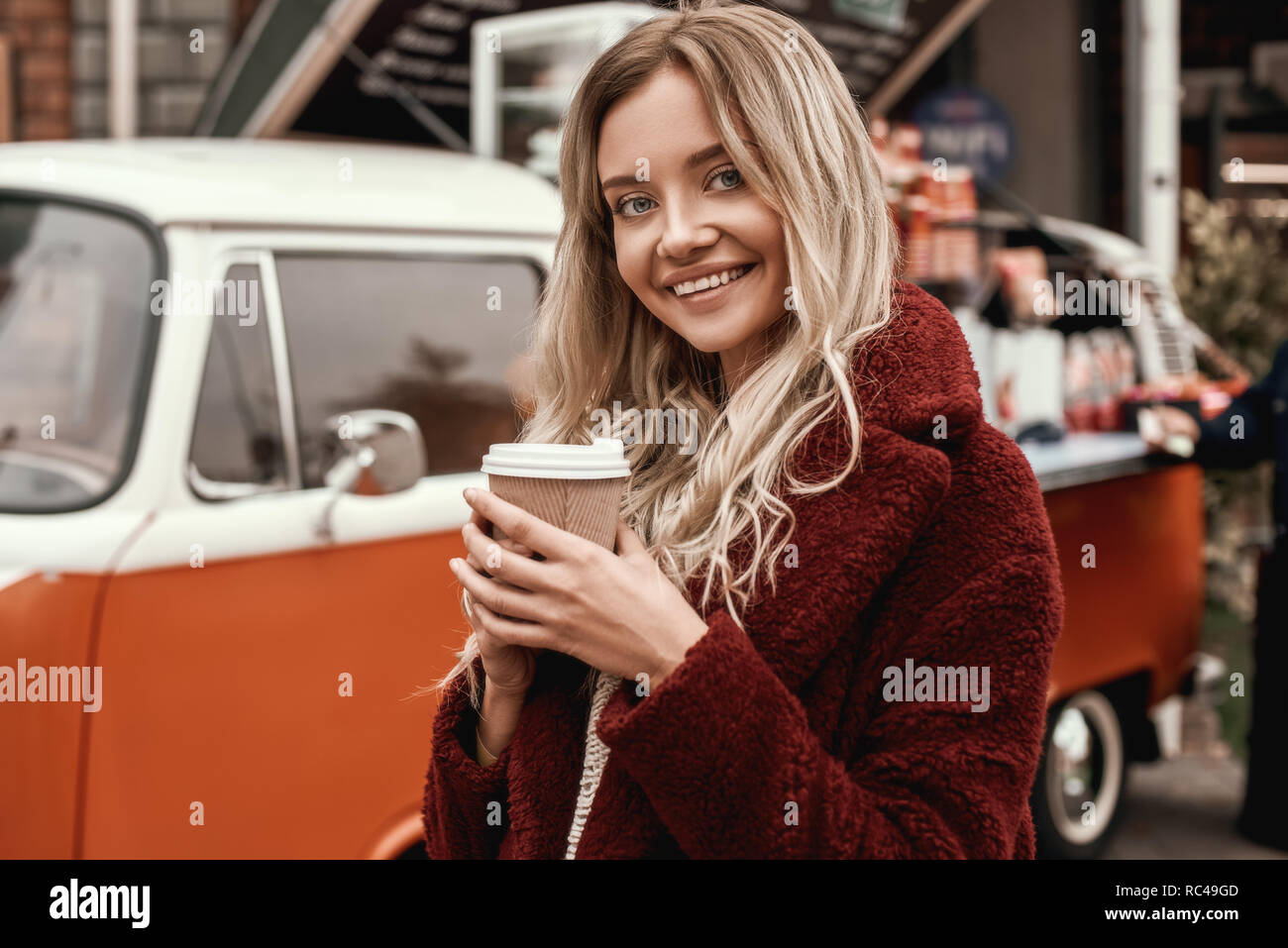 Kaffee trinken im Freien. Blonde schöne weiße Frau mit langem Haar mit schüchternen Lächeln auf städtischen Hintergrund und Kaffee zu trinken. Outdoor Foto von lov Stockfoto