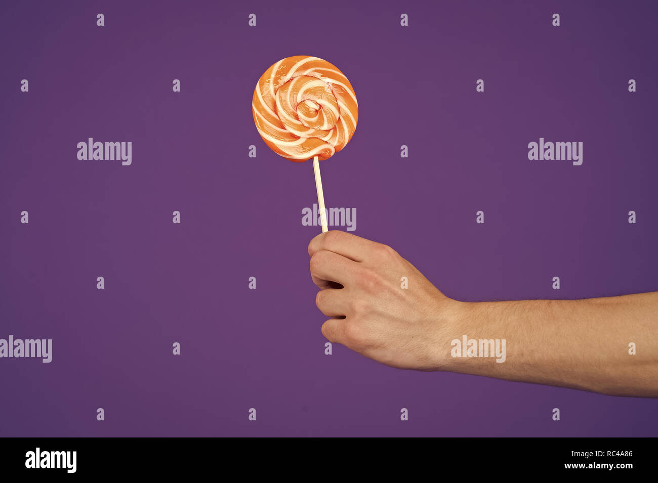 Lutscher in der Hand auf violett unterlegt. Candy auf Stick auf lila Hintergrund. Süßigkeiten Swirl. Essen oder Snacks und Dessert essen. Sweet Shop Konzept, kopieren. Stockfoto