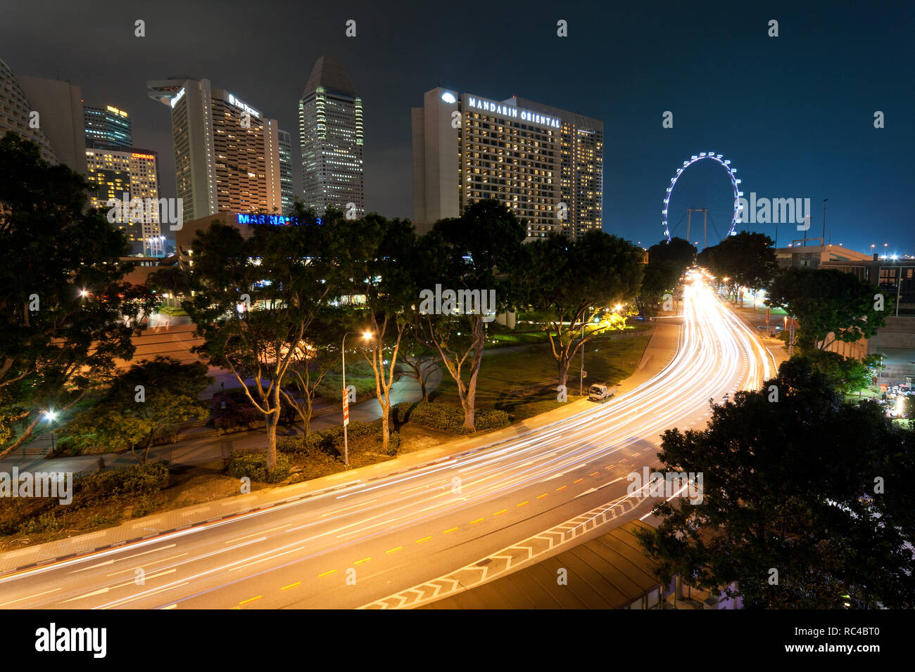 Der Verkehr in leichten Wanderwegen zum Singapore Flyer, ein gigantisches Riesenrad, in Singapur in der Abenddämmerung. Mehrere berühmte Hotels sind im Hintergrund. Stockfoto