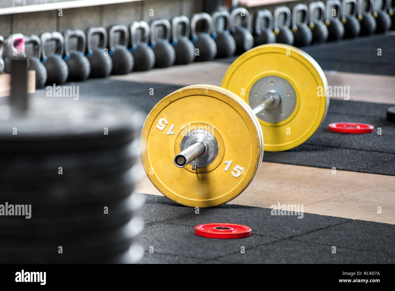 Gelbe barbell auf dem Boden in der Turnhalle, gesehen von der Seite in selektiven Fokus. Schwere Gewichte Training Ausrüstung Stockfoto