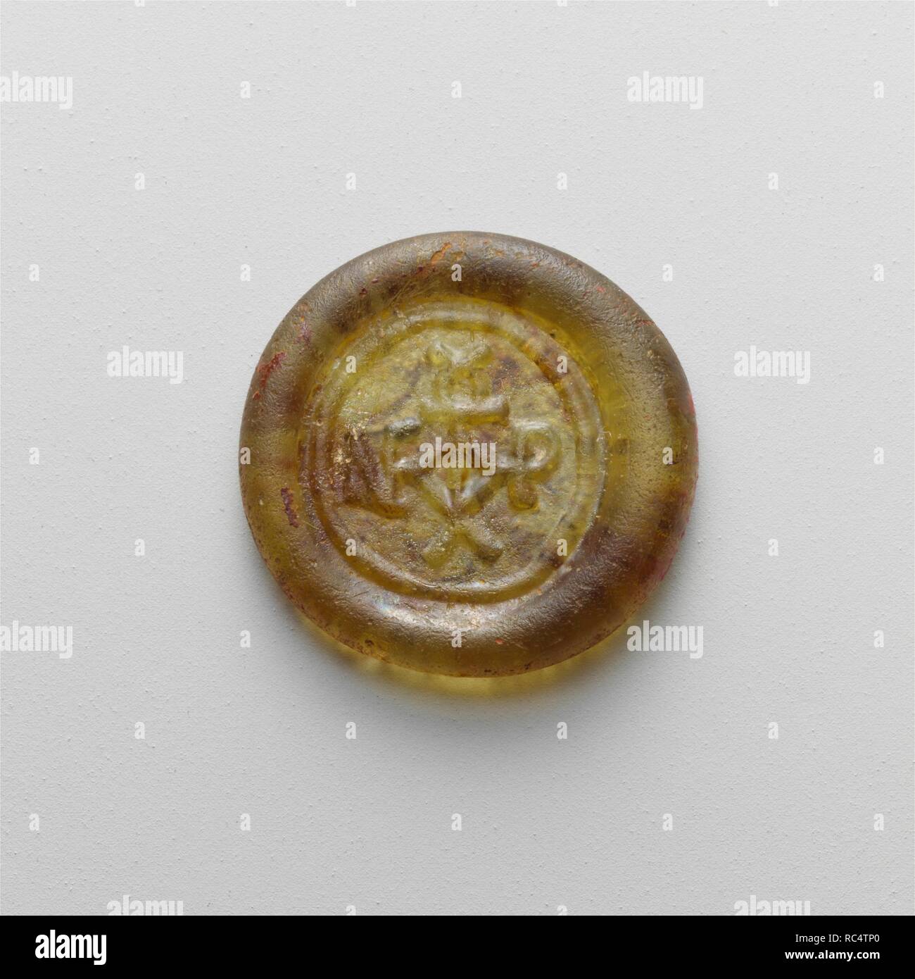 Glas Gewicht. Kultur: Roman. Abmessungen: 13/16 × 1/8 in., 0.1Oz. (2,1×0,3 cm, 2 g). Datum: 6.-7. Jh. N.CHR.. Durchsichtig gelb grün. Runde Platte mit der abgerundeten Kante; beeindruckt Oberfläche; flachen Boden. Auf der Vorderseite, Stempel in Flachrelief, bestehend aus einem kreuzförmigen Monogramm, durch eine Linie umgeben. Intakt; Mattierung und Lochfraß, mit Spuren von bräunlich Verwitterung. Das Gewicht ist mit einem griechischen Monogramm, seine Authentizität zu garantieren. Solche kleinen Glas Gewichte wurden von den Byzantinern und später von den Arabern verwendet, um den Wert von Gold- und Silbermünzen zu prüfen. Dieses Beispiel wiegt die e Stockfoto