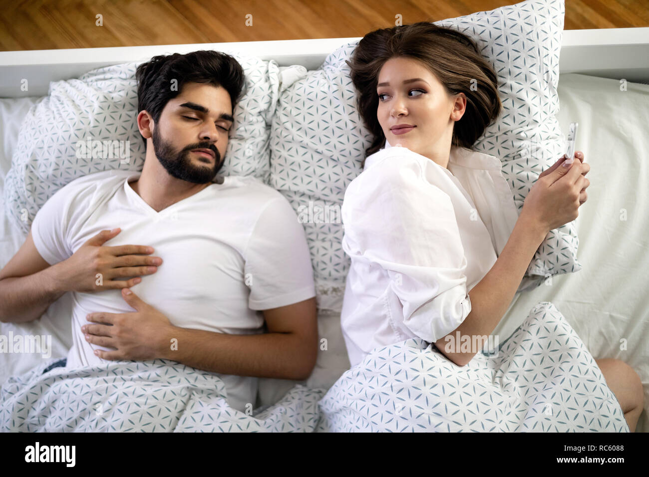 Schöne junge Frau sms mit Liebhaber auf dem Smartphone während Mann schläft Stockfoto
