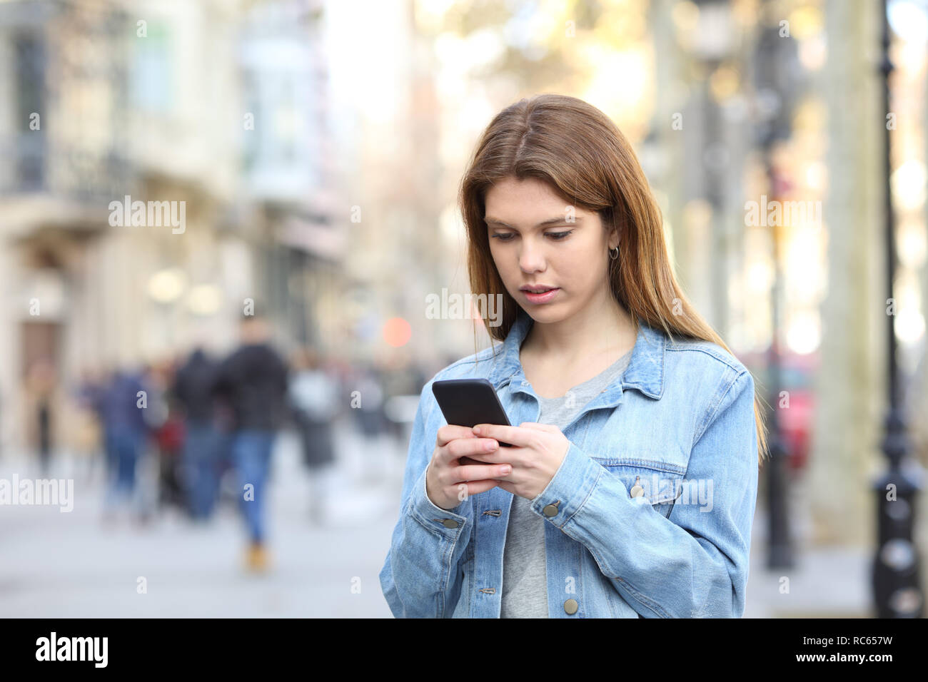 Ernsthafte Jugendmädchen SMS-Nachrichten auf dem Smartphone zu Fuß auf der Straße Stockfoto