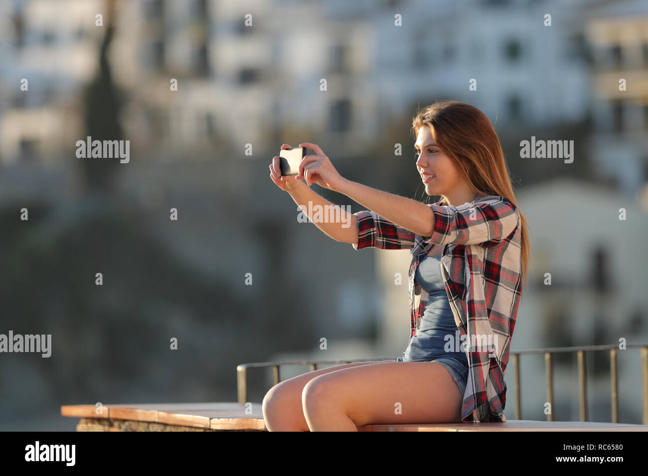 Happy Teenager Fotos mit einem smart phone Sitzen auf einem Felsvorsprung in der Stadt Stadtrand Stockfoto