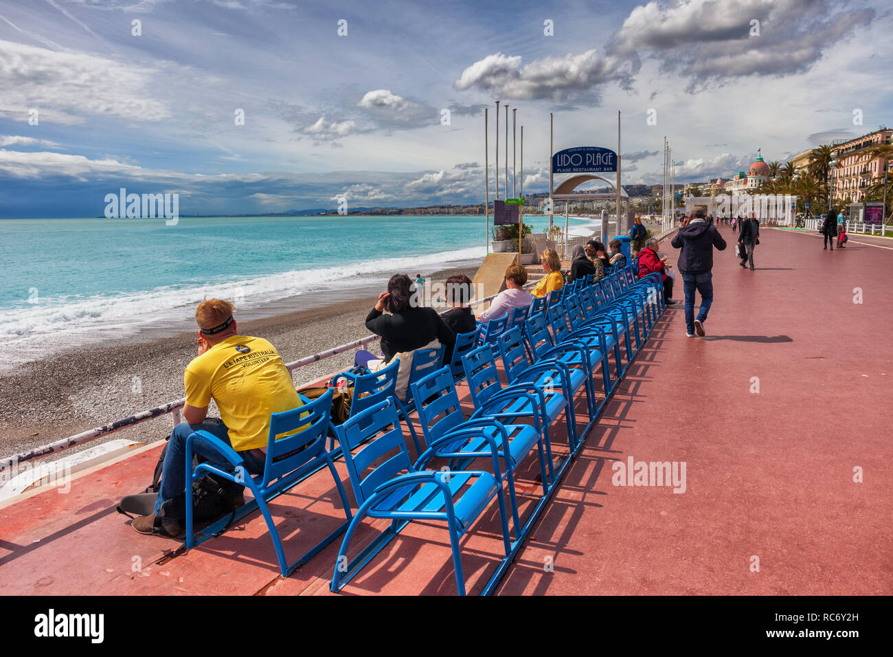 Stadt Nizza in Frankreich, Menschen entspannen am Meer an der Promenade des Anglais und blaue Stühle auf Französische Riviera - Cote d'Azur Stockfoto