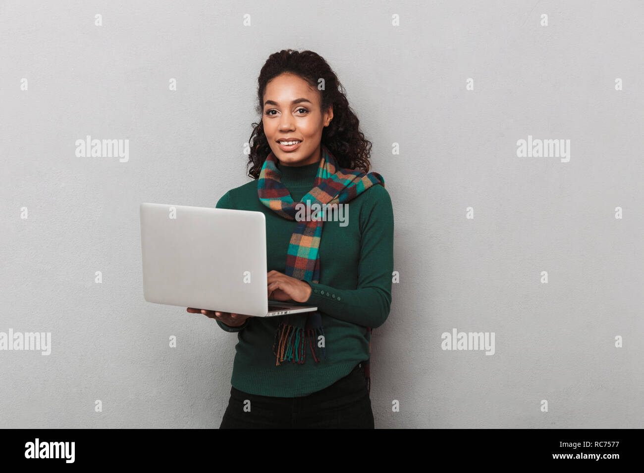 Fröhlich afrikanische Frau mit Kopftuch stehend über grauen Hintergrund isoliert, Laptop Stockfoto