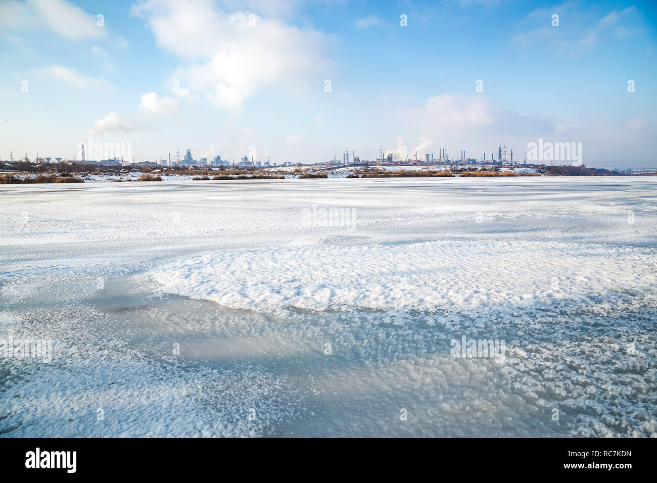 Metallurgie Anlage mit Rauch aus dem Ufer von einem gefrorenen See aus gesehen. Stahl Werk mit Smog auf Wintertag. Ökologie Probleme, Luftverschmutzung. Stockfoto
