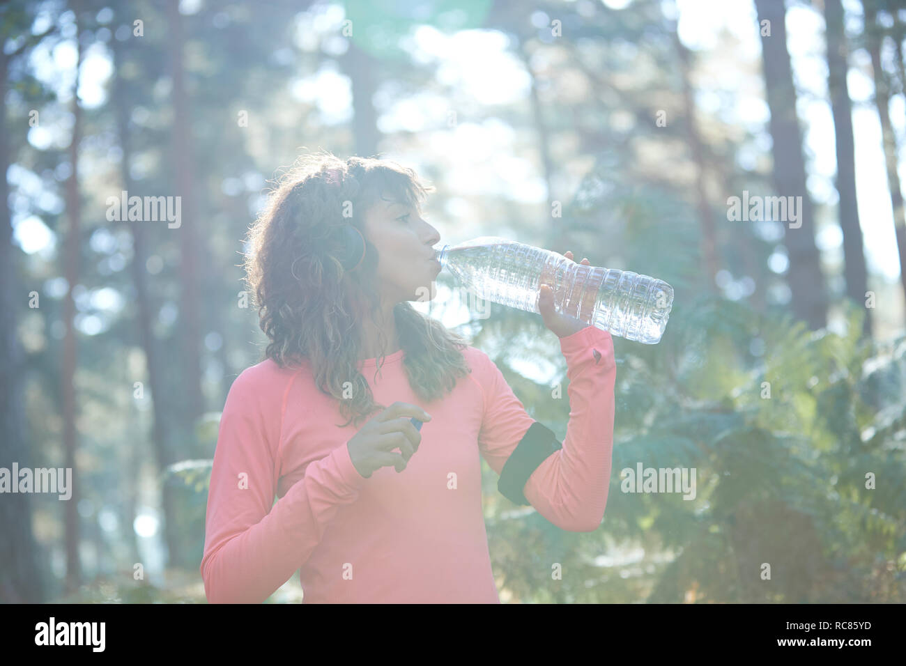 Junge weibliche Läufer trinken Mineralwasser in sonnendurchfluteten Wald Stockfoto