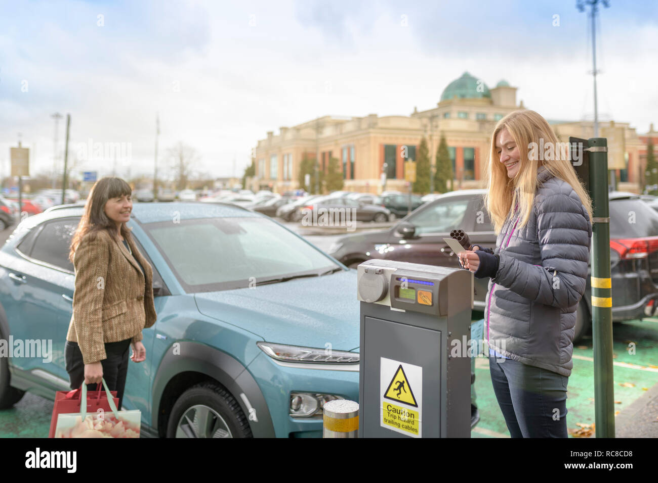 Weibliche Käufer laden Elektroauto am Point, Manchester, UK Stockfoto