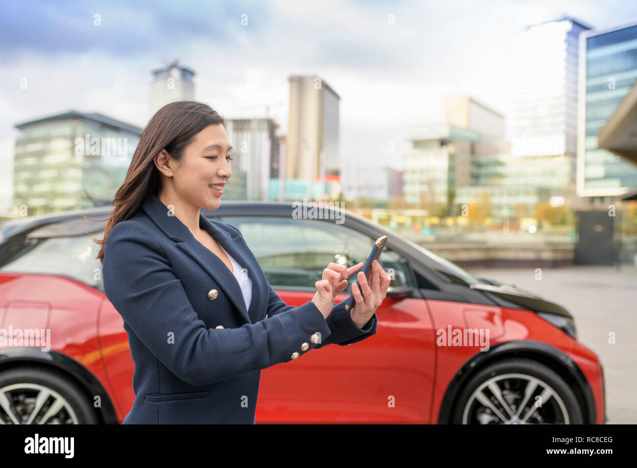 Frau prüfen elektrische Auto kostenlos auf Handy app, Manchester, UK Stockfoto