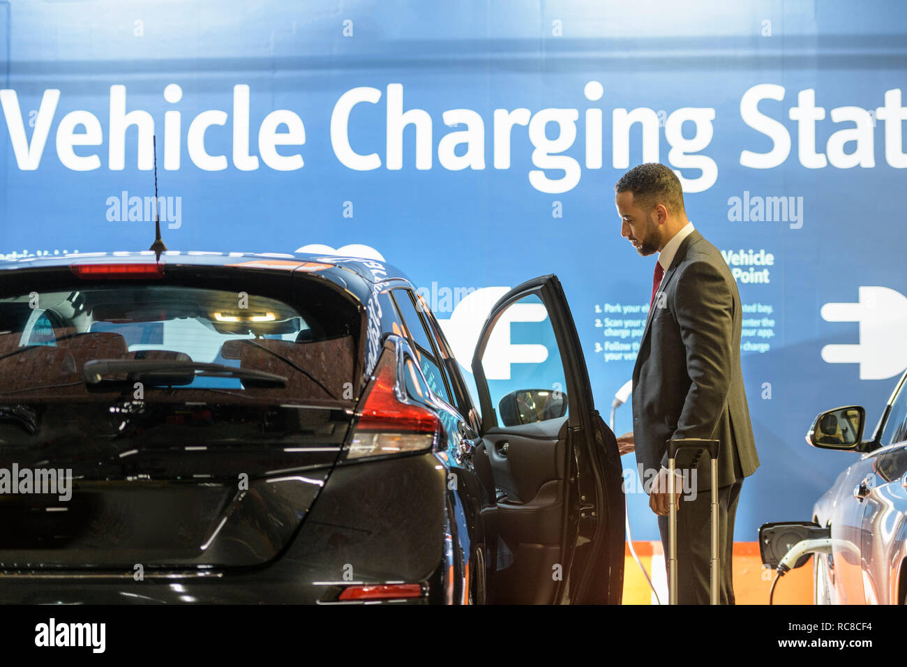 Geschäftsmann öffnet Tür für elektrische Fahrzeug auto Elektrofahrzeug Ladestation, Manchester, UK Stockfoto