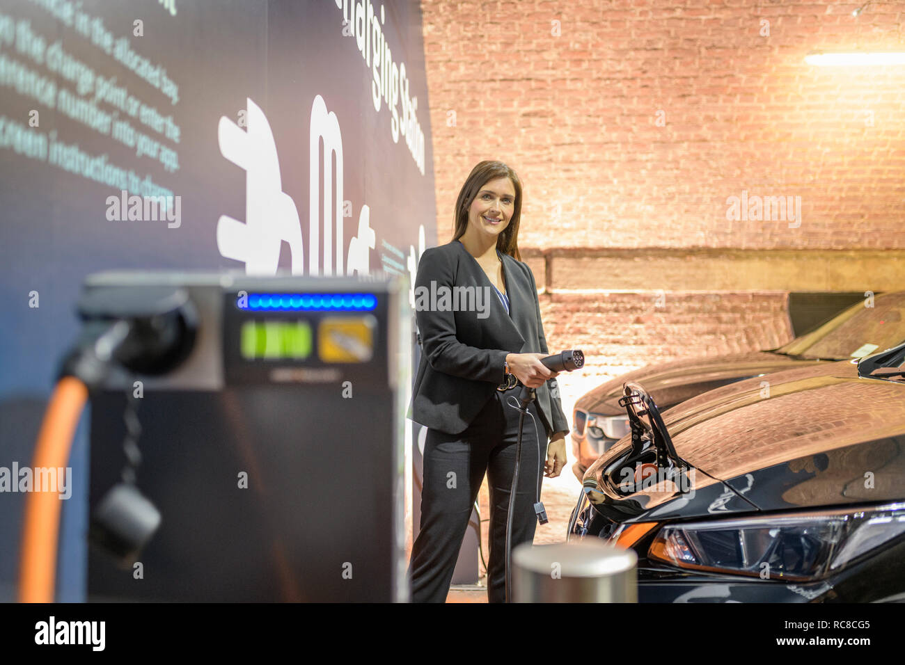 Portrait der Unternehmerin am Elektrofahrzeug Ladestation, Manchester, UK Stockfoto